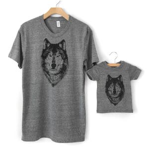 Puede incluir: Un conjunto de dos camisetas grises con una ilustraci&oacute;n de lobo en blanco y negro. La camiseta m&aacute;s grande tiene una ilustraci&oacute;n de lobo m&aacute;s grande y la camiseta m&aacute;s peque&ntilde;a tiene una ilustraci&oacute;n de lobo m&aacute;s peque&ntilde;a.