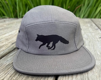Puede incluir: Una gorra gris de 5 paneles con una silueta negra de un zorro corriendo en la parte delantera.