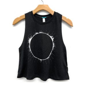 Woman's black, racerback cropped tank top that is hand screen printed with a total solar eclipse design on the front in white ink. Shirt by Little Lark