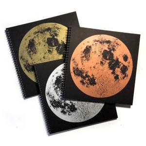 May include: Three spiral bound notebooks with black covers and a full moon image on each. The moons are printed in gold, copper, and silver foil.
