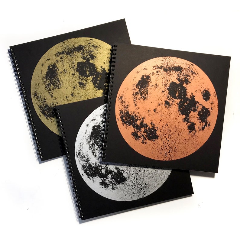 May include: Three spiral bound notebooks with black covers and a full moon image on each. The moons are printed in gold, copper, and silver foil.
