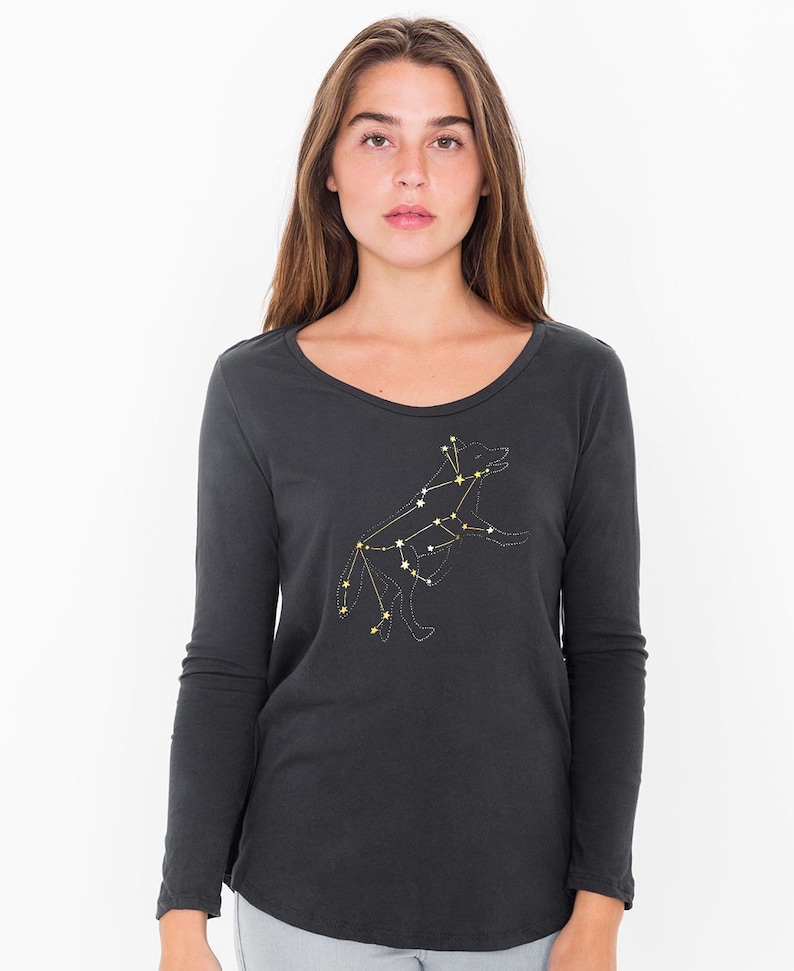 May include: Dark gray long-sleeve shirt with a scoop neck. The shirt features a constellation design of a dog, with white and yellow star accents. The dog constellation is on the front of the shirt.