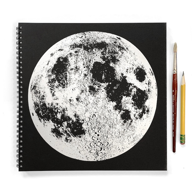May include: A black spiral bound notebook with a white image of the moon on the front cover.