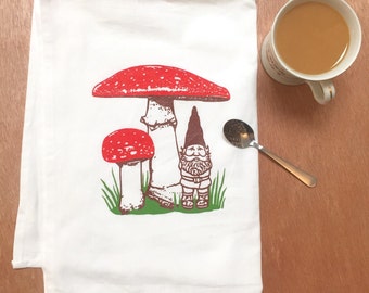 Peut inclure: Serviette de cuisine blanche avec une illustration de champignon rouge et blanc et un gnome brun. Le gnome porte un chapeau rouge et a une barbe blanche.