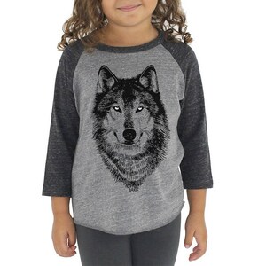 Puede incluir: Una camiseta de manga raglan gris y negra con una ilustraci&oacute;n de lobo en blanco y negro en la parte delantera. El texto "WILD" est&aacute; impreso debajo del lobo.
