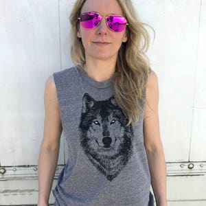 Puede incluir: Una camiseta gris sin mangas con un estampado gr&aacute;fico de lobo en blanco y negro. La modelo lleva gafas de sol de espejo rosa.