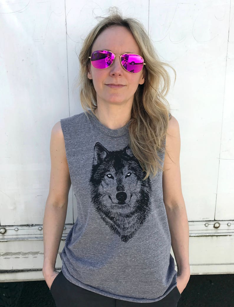 Puede incluir: Una camiseta gris sin mangas con un estampado gr&aacute;fico de lobo en blanco y negro. La modelo lleva gafas de sol de espejo rosa.