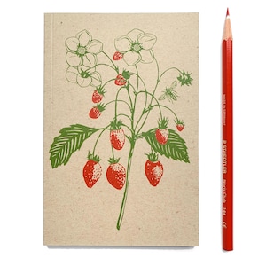 Op de afbeelding: Een notitieboek met een illustratie van een aardbeienplant in groen en rood. Een rode potlood ligt naast het notitieboek. Het notitieboek heeft een beige kaft en de potlood is gemarkeerd met "Made in Germany".