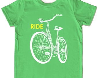 May include: A lime green t-shirt featuring a white bicycle illustration. The word "RIDE" is printed in yellow above the bicycle. The bicycle design includes handlebars, a seat, and wheels.