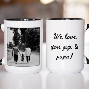 May include: White ceramic mug with a black interior and handle. One side features a black and white photo of a family walking. The other side has the text "We love you gigi & papa!" in black script.