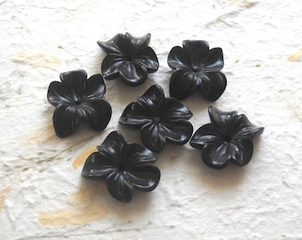 Puede incluir: Seis cuentas negras con forma de flor, cada una con cinco pétalos y un pequeño agujero en el centro.