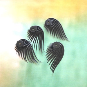 Puede incluir: Cuatro adornos negros en forma de pluma con un agujero redondo en el centro. Los adornos están hechos de un material flexible y tienen una superficie texturizada.