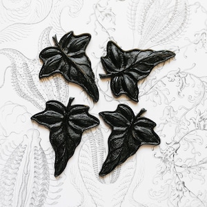 May include: Four black ivy leaf-shaped wall decor pieces, each with a distinct vein pattern, arranged on a white background with a black and white floral design.