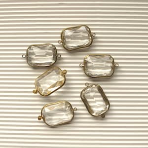 May include: Six clear glass rectangular beads with brass accents. The beads have a faceted design and are strung on a wire.