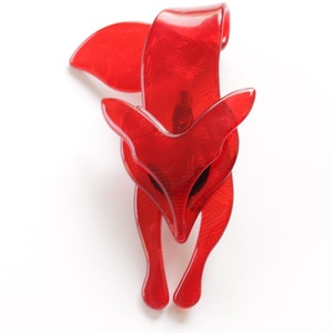 Puede incluir: Un broche de zorro de pl&aacute;stico rojo. El zorro est&aacute; en posici&oacute;n de cuclillas con la cabeza inclinada hacia abajo. El broche tiene una superficie texturizada.