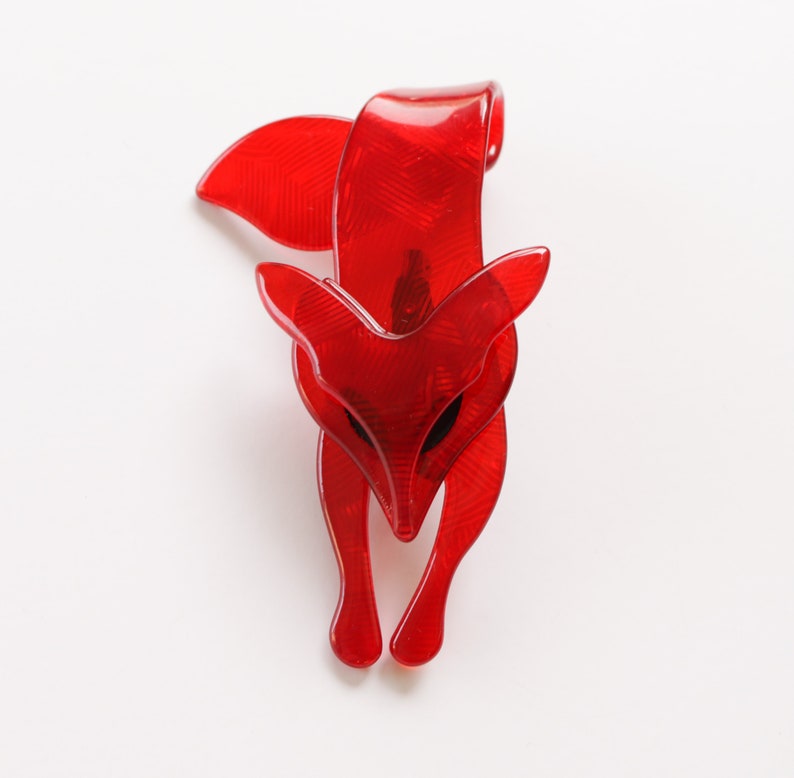 Puede incluir: Un broche de zorro de pl&aacute;stico rojo con un dise&ntilde;o detallado. El zorro est&aacute; mirando hacia adelante con la cabeza inclinada hacia abajo.