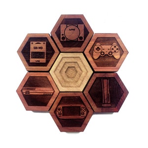 May include: A set of six hexagonal wooden coasters with different video game console and controller designs. The coasters are made of dark wood with a light wood center.