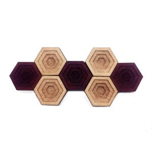 May include: A set of six hexagonal wooden coasters in two shades of brown. The coasters are arranged in a row, alternating colors.
