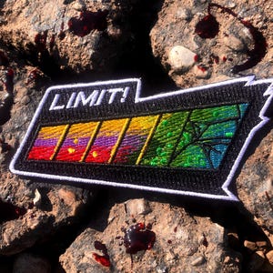 May include: A black and white embroidered patch with the word "LIMIT!" in white text. The patch features a rainbow-coloured bar graph with a green and black spider web design.