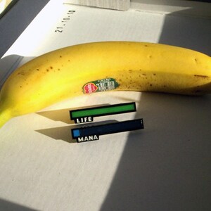 May include: A yellow banana with a green sticker on it.  Two progress bars are below the banana, one green labeled "LIFE" and one blue labeled "MANA".
