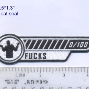 Op de afbeelding: Geborduurde patch met de tekst "FUCKS" en een voortgangsbalk met "0/100". De patch heeft een zwart-wit ontwerp met een persoon in een cirkel. De patch meet 11,4 x 3,3 cm en is hitteverzegeld.
