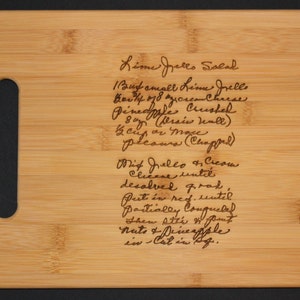 May include: A close-up of a wooden cutting board with a handwritten recipe for Lime Jello Salad. The recipe includes ingredients like lime jello, cream cheese, pineapple, and whipped cream.