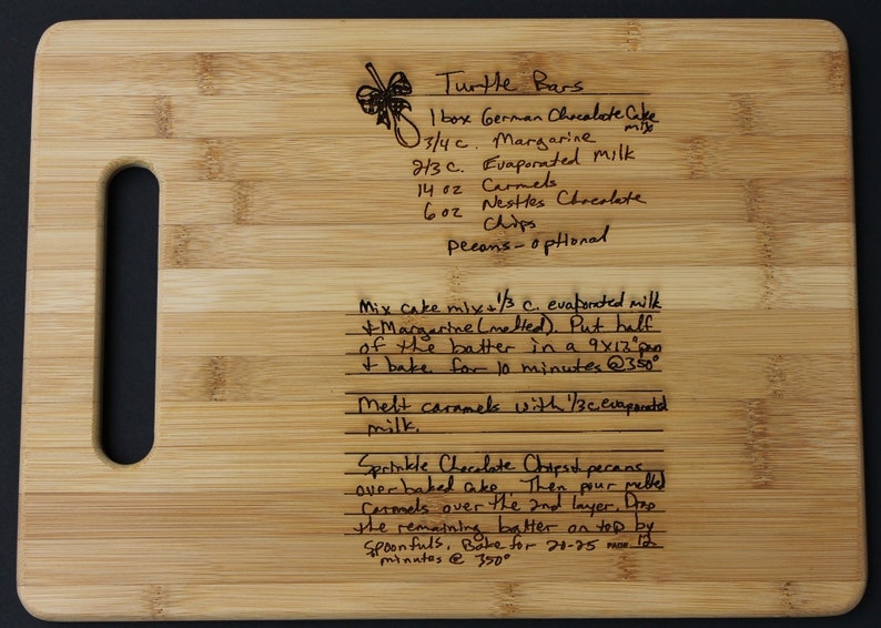 May include: A close-up of a wooden cutting board with a handwritten recipe for Turtle Bars. The recipe includes ingredients like German chocolate cake mix, margarine, evaporated milk, caramels, and chocolate chips. The recipe also includes instructions for baking the bars.