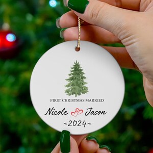 Puede incluir: Adorno navideño redondo blanco con un árbol de Navidad verde acuarela y el texto "First Christmas Married Nicole & Jason ~2024~" con dos corazones rojos.