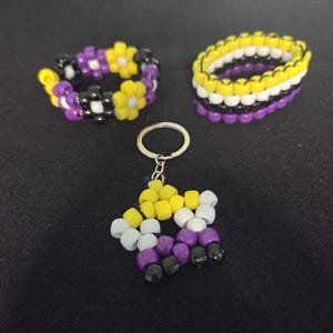 Peut inclure: Trois accessoires perl&eacute;s : un porte-cl&eacute;s et deux bracelets. Le porte-cl&eacute;s est en forme d'&eacute;toile et les bracelets sont ronds. Les perles sont jaunes, blanches, violettes et noires. Les bracelets ont un motif floral.