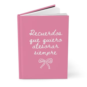 May include: A pink journal with the words "Recuerdos que quiero atesorar siempre" in white script, along with a bow illustration. The journal is open, revealing white pages.