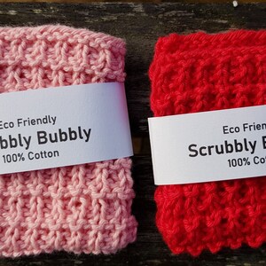 May include: Two knitted dishcloths, one pink and one red, with a white label that reads "Eco Friendly Scrubby Bubbly 100% Cotton".