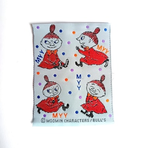 May include: A white fabric patch with four colorful illustrations of a character named "Myy" from the Moomin series. The patch has a blue border and the text "Moomin Characters/Bull's" at the bottom.