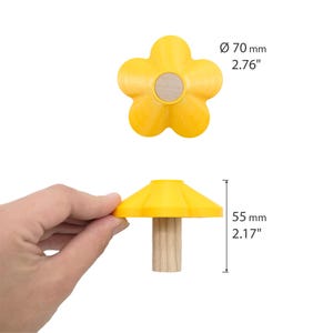 May include: A yellow flower-shaped knob with a light wood center. The top view shows a diameter of 2.76 inches. The side view shows a height of 2.17 inches, featuring a yellow conical top attached to a cylindrical light wood base.
