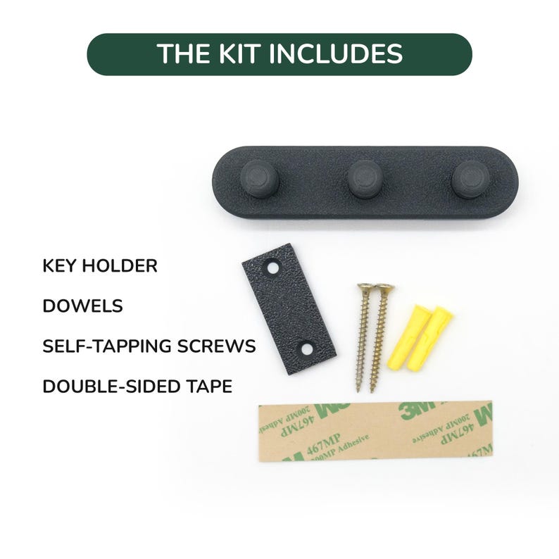 May include: A black key holder with three pegs, a mounting plate, screws, dowels, and double-sided tape. The text "THE KIT INCLUDES" is at the top. The kit includes all the necessary hardware for installation.