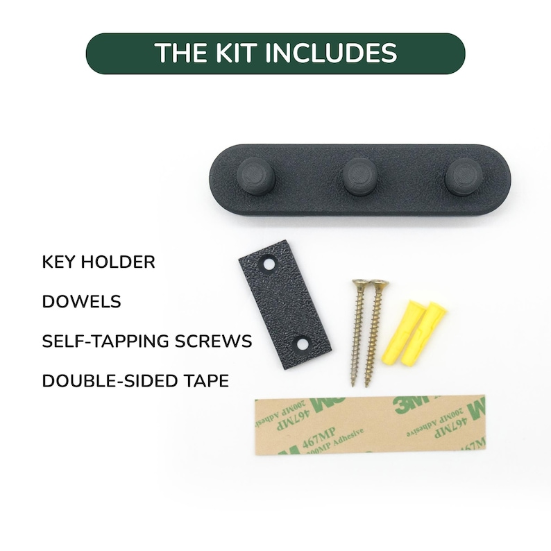May include: A black key holder with three pegs, a mounting plate, screws, dowels, and double-sided tape. The text "THE KIT INCLUDES" is at the top. The kit includes everything needed for installation.