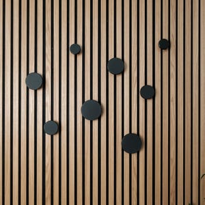 May include: A wall with vertical wooden slats in a light wood tone with black accents. There are nine black round knobs attached to the wall.