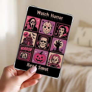 May include: A rectangular black tablet case featuring a grid of eight pink and purple horror-themed illustrations, including a ghost mask, hockey mask, vampire, haunted house, Frankenstein, zombie hand, television, pumpkin, and doll. Text reads Watch Horror Read Smut.