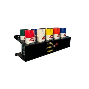 May include: A black metal spray paint can organizer holding several cans of spray paint. The cans are various colors, including red, white, yellow, blue, and green. The organizer has a two-tiered design and features the text "ACE PREMIUM".