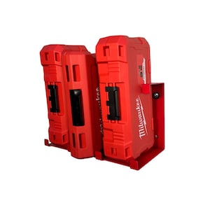 May include: A red Milwaukee power tool battery holder with two battery cases. The cases are red with black latches and the Milwaukee logo. The holder is made of red metal and is designed to hold the batteries securely.