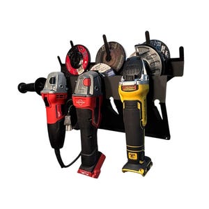 May include: A black metal wall-mounted storage rack with four slots for holding angle grinders and abrasive discs. Three angle grinders are hanging on the rack, one red, one black, and one yellow. The rack has a black powder-coated finish.