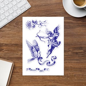 May include: A sticker sheet featuring blue ink illustrations of a rose, a winged cherub aiming a bow and arrow, a flying dove, and two ribbons. One ribbon displays the text Memento vivere, and the other ribbon displays the text Memento mori.