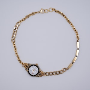 May include: A gold-tone watch with a white face and black hands attached to a gold chain bracelet.