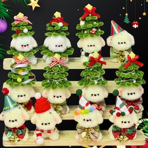 May include: A collection of plush dog figurines, each adorned with festive Christmas tree costumes and holiday accessories. The dogs are white with black button eyes and are arranged on wooden shelves. Decorations include red bows, hats, and bells.