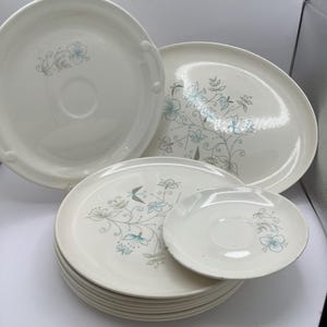 May include: A set of white ceramic plates with a blue and grey floral pattern. The set includes a large platter, a smaller platter, and several dinner plates and a saucer.