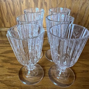 May include: Set of six clear glass drinking glasses with a fluted design and a floral pattern. The glasses have a stemmed base.