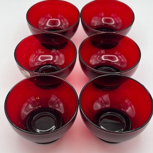 May include: Six red glass bowls with a glossy finish. Each bowl has a dark red interior and a black rim. The bowls are arranged in two rows of three against a white background. The bowls are likely for serving food.