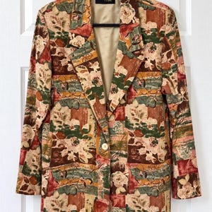 Könnte beinhalten: Ein langärmeliger Blazer mit einem mehrfarbigen Blumen- und geometrischen Blockmuster in Rost, Olivgrün, Creme und Braun. Das Kleidungsstück verfügt über ein steigendes Revers, einen einzelnen Knopfverschluss vorne und ein beiges Innenfutter.