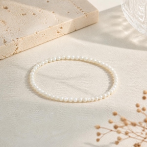 May include: A delicate bracelet composed of a single strand of small, uniform, round white pearls. The pearls are strung together in a circular shape, showcasing a smooth, lustrous finish and a consistent size throughout the entire piece of jewelry.