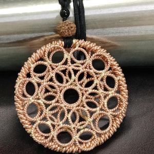 May include: A copper wire pendant necklace with a circular design featuring a repeating pattern of interwoven circles. The pendant is a light copper color and has a delicate, intricate design.