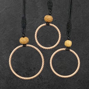 May include: Three gold-colored rope rings with black cords and brown wooden beads hanging from them.